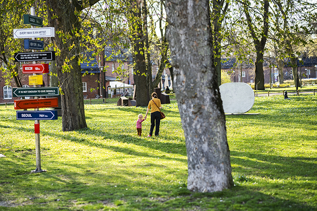 En vuxen och ett litet barn går hand i hand i en grönskande park.