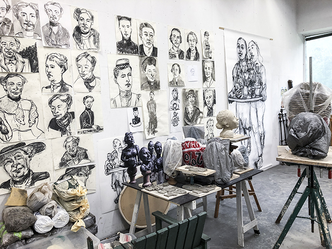 Astrid Göransson's studio with several drawn portraits on the walls. On a table are small bronze sculptures representing women.
