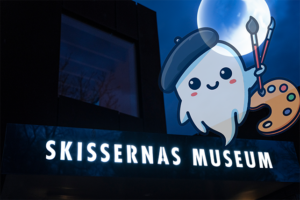 Skissernas Museums fasad när det är mörkt ute. I ena hörnet ser vi ett tecknat spöke. På himmelen en fullmåne.
