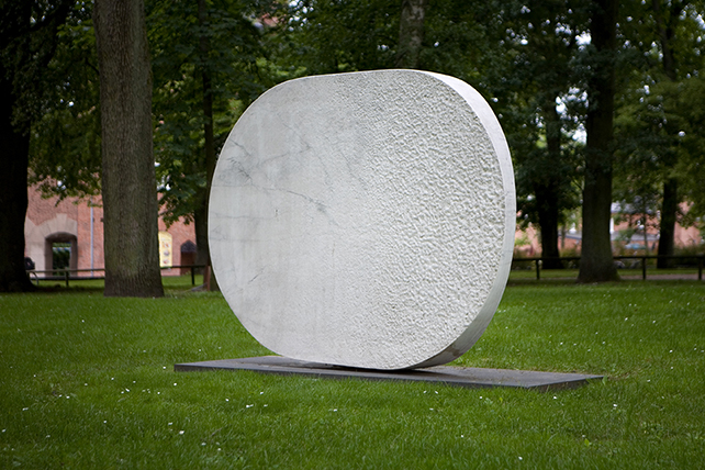 Skulptur, stor rund stenskiva stående på höjden.