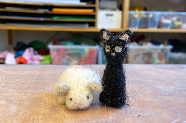 Två små nåltovade figurer på ett bord. En svart katt och en vit mus.