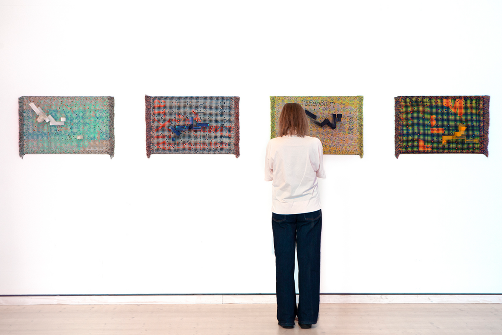 Fyra konstverk hänger på en vägg, en besökare tittar på konsten.