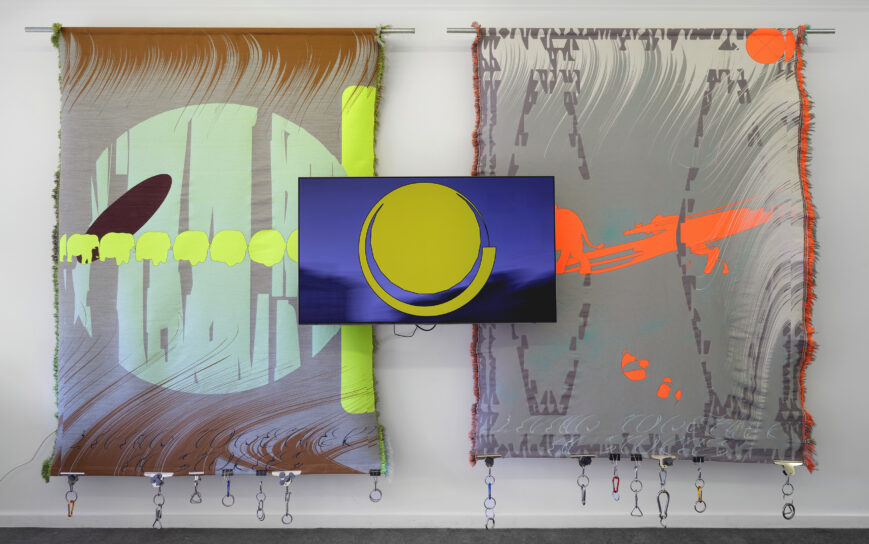 Triptyk två vävar hänger på en vägg och i mitten en digital skärm. 