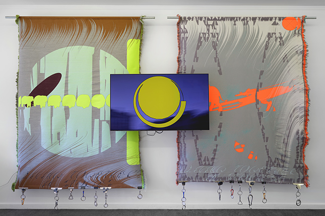 Triptyk, två vävar hänger på en vägg , mellan dem en video.