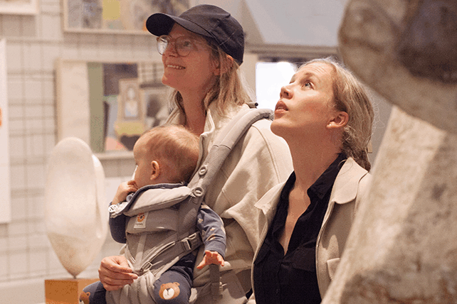 Två vuxna tittar upp på ett konstverk utanför bilden. Den ena har ett litet barn i bärsele på magen.