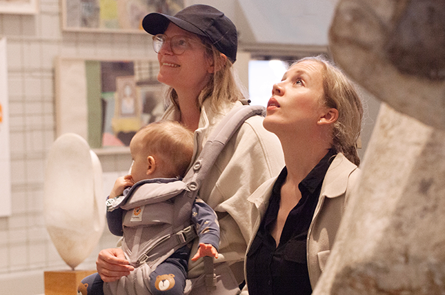 Två vuxna tittar upp på ett konstverk utanför bilden. Den ena har ett litet barn i bärsele på magen.