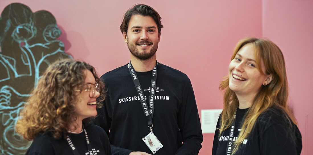 Tre museivärdar står i en grupp och pratar och skrattar. 