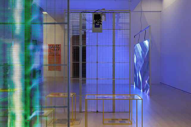 Installationsvy i utställningen Kodade trådar, i förgrunden en lysande digital skärm med grönt ljus, på avstånd en digital skärm med blått ljus.