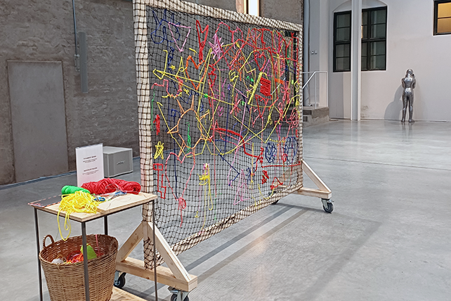 En stor vävram bredvid står ett bord där det ligger garnnystan.