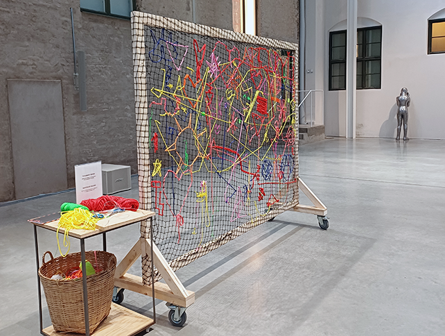 En stor vävram bredvid står ett bord där det ligger garnnystan.