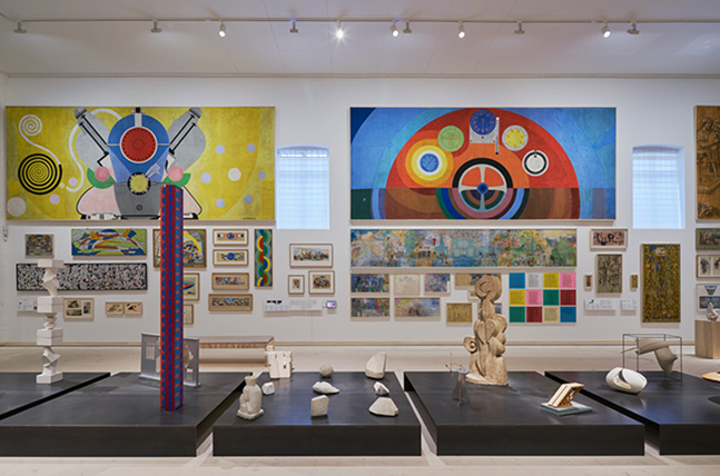 Internationella salen på Skissernas Museum, låga podier med skulpturer, i bakgrunden flera målningar på en vägg.