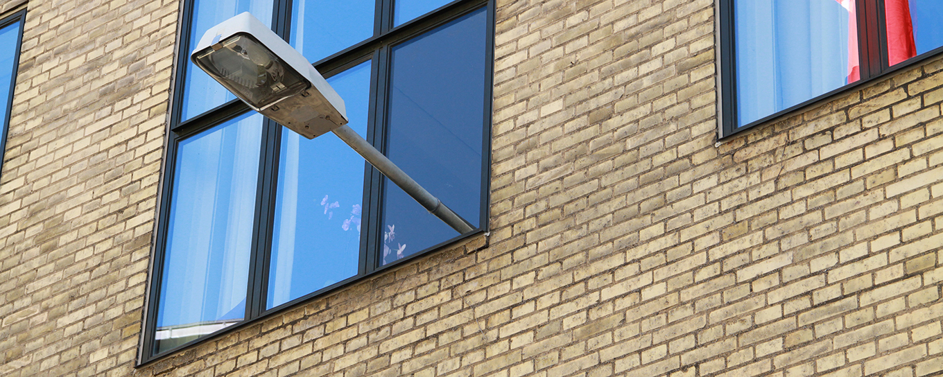 En gatlampa sticker ut från ett fönster på en gul tegelfasad.