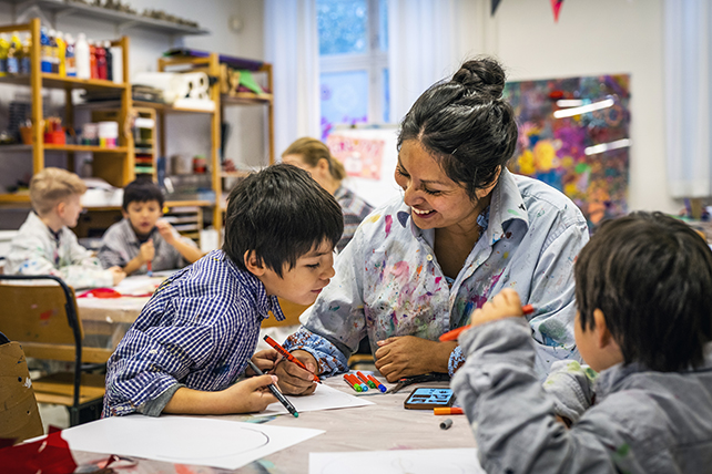 Två barn och en vuxen sitter vid ett bord och tittar på något som en av dem ritat.