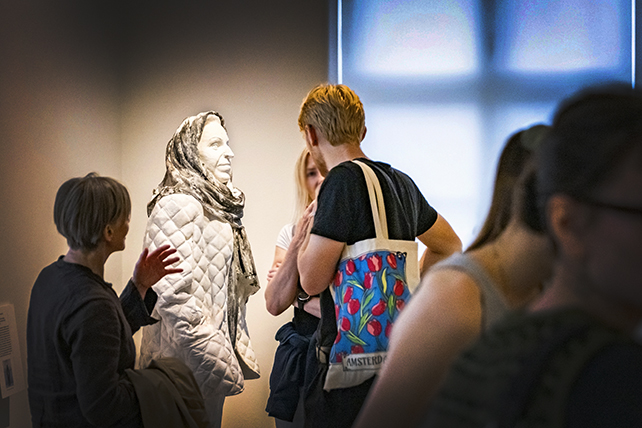 Människor i ett rum står samlade framför en skulptur föreställande skådespelaren Margaretha Krook.