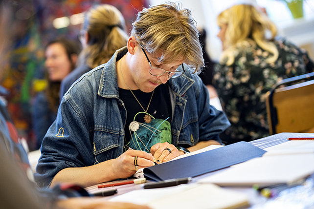 En person sitter vid ett bord och tecknar.