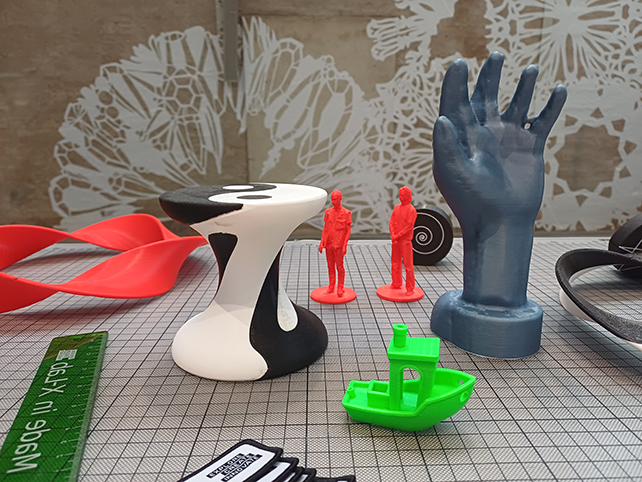3D-printade föremål på ett bord. En hand, en båt, två små människor.
