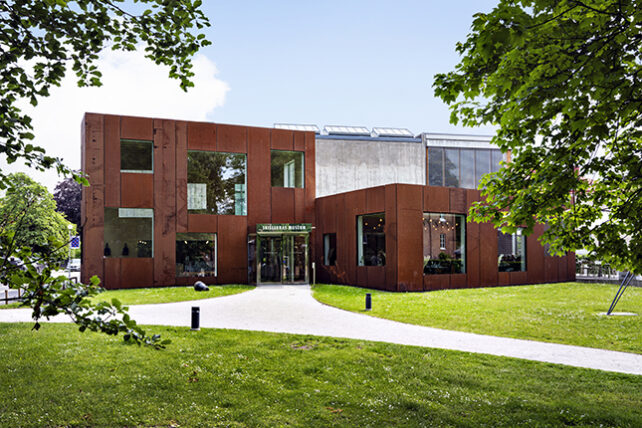 Skissernas Museums fasad, sommar bild med grönt gräs och bladverk i förgrunden.